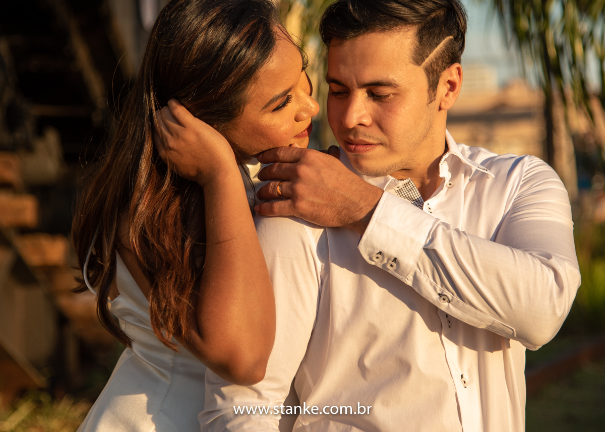 Ensaio pós casamento de Giseli e Aurélio, A Giseli abraçando o ele por trás e outra mão segurando os cabelos ele levando mão no rosto dela, e ambos sorrindo. Fotos feitas no Memorial Ferroviário, em Campo Grande-MS, por Pedro Stanke.