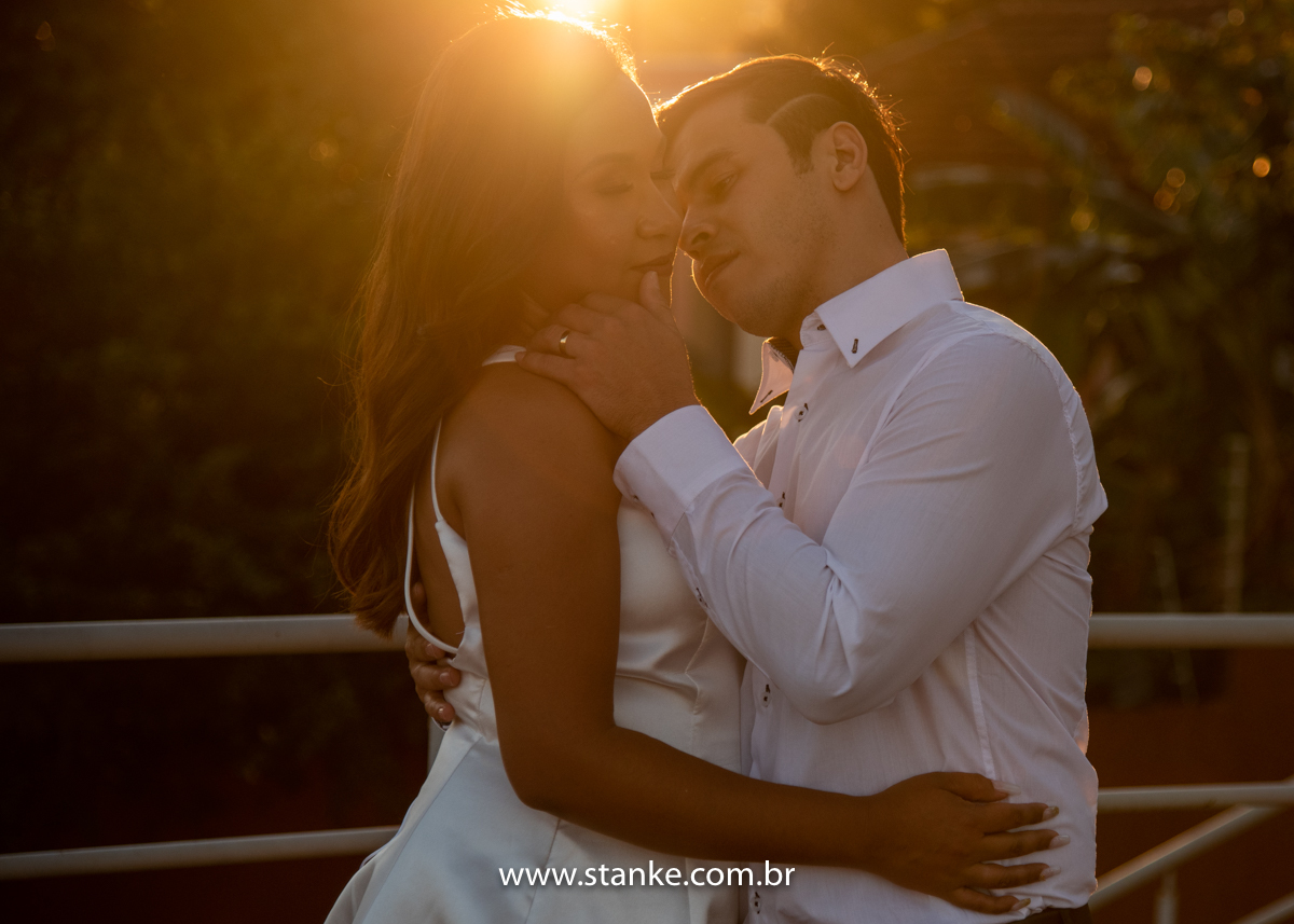 Ensaio pós casamento de Giseli e Aurélio, Giseli de olhos fechados ganhando um carinho do Aurélio no rosto da Giseli e raios do por do sol ao fundo. Fotos feitas no Memorial Ferroviário, em Campo Grande-MS, por Pedro Stanke.