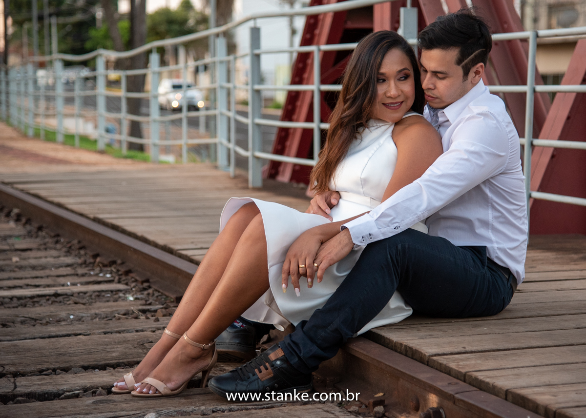 Ensaio pós casamento de Giseli e Aurélio, Sentados sobre o viaduto dos trilhos e Giseli sendo abraçada por trás e olhando para Aurélio de mãos dadas. Fotos feitas no Memorial Ferroviário, em Campo Grande-MS, por Pedro Stanke