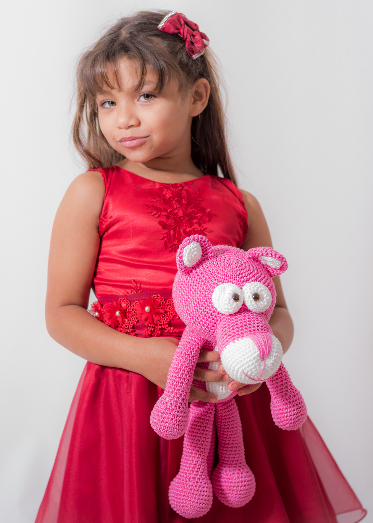 Ensaio em estúdio da Júlia 09 anos, Segurando com as mãos juntas uma boneca pantera cor de rosa feita de crochê, muito fofinha. E olhando para câmera meio de lado.. Fotos feitas em Campo Grande-MS, pelo fotógrafo Pedro Stanke.