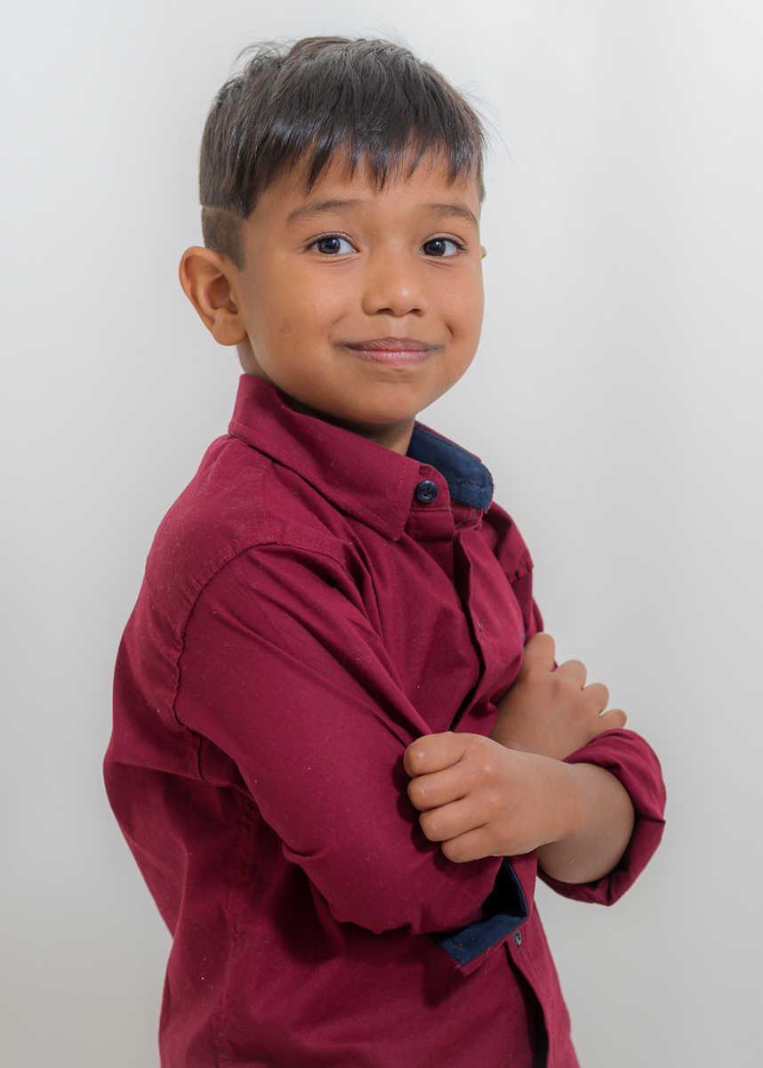 Ensaio Artur, de 07 anos, com a sua camisa vermelha. De lado com os braços cruzados e olhando para a câmera, Fotos feitas em Campo Grande-MS, pelo fotógrafo Pedro Stanke.