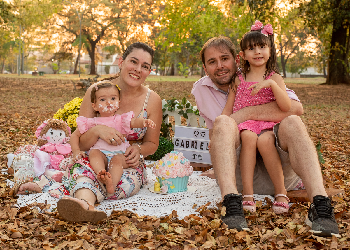 Smash the Cake da Gabriella e sua família todos posando para as fotos junto ao bolo após se lambuzar e no fundo super iluminado pelo sol refletindo nas árvores. Fotos feitas pelo fotógrafo Pedro Stanke em Campo Grande-MS. 