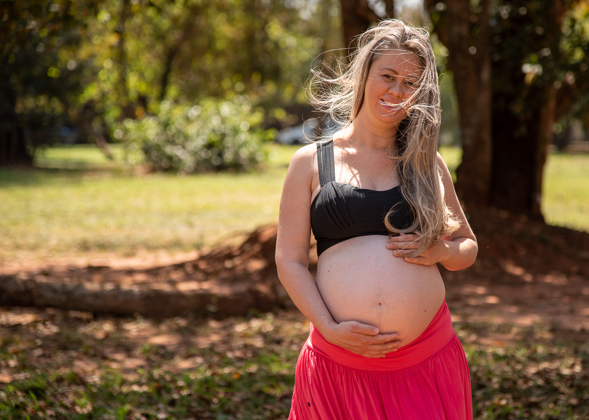 Ensaio de gestante de Gisele e Everton, a gestante com uma saia laranja e um top preto, de pé com as  mãos na barriga  e vento bagunçando os cabelos. Fotos feitas pelo fotógrafo Pedro Stanke, em Campo Grande-MS. 