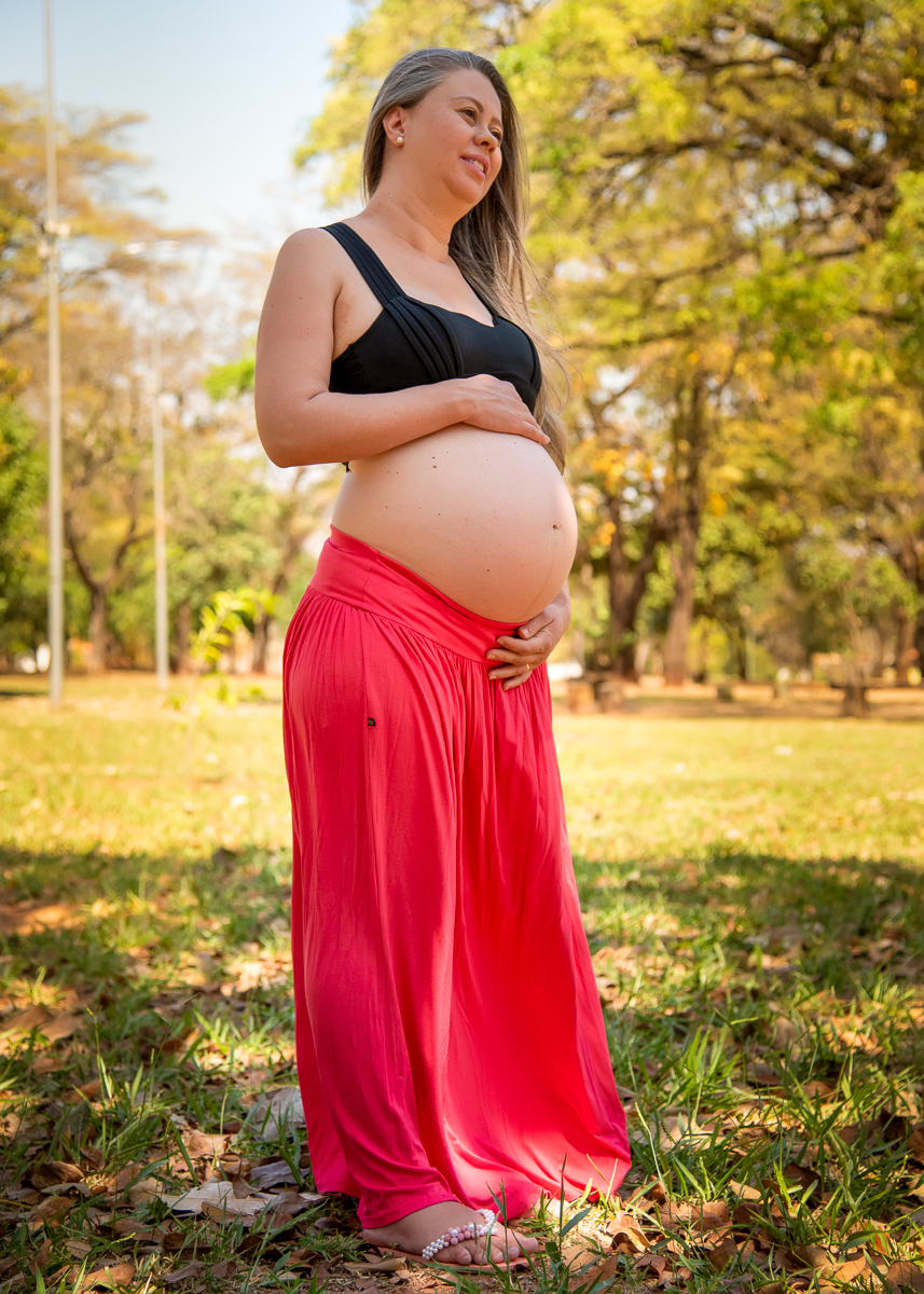 Ensaio de gestante de Gisele e Everton, foto de corpo inteiro, a gestante com uma saia laranja e um top preto, de pé com as  mãos na barriga olhando para frente. Fotos feitas pelo fotógrafo Pedro Stanke, em Campo Grande-MS. 