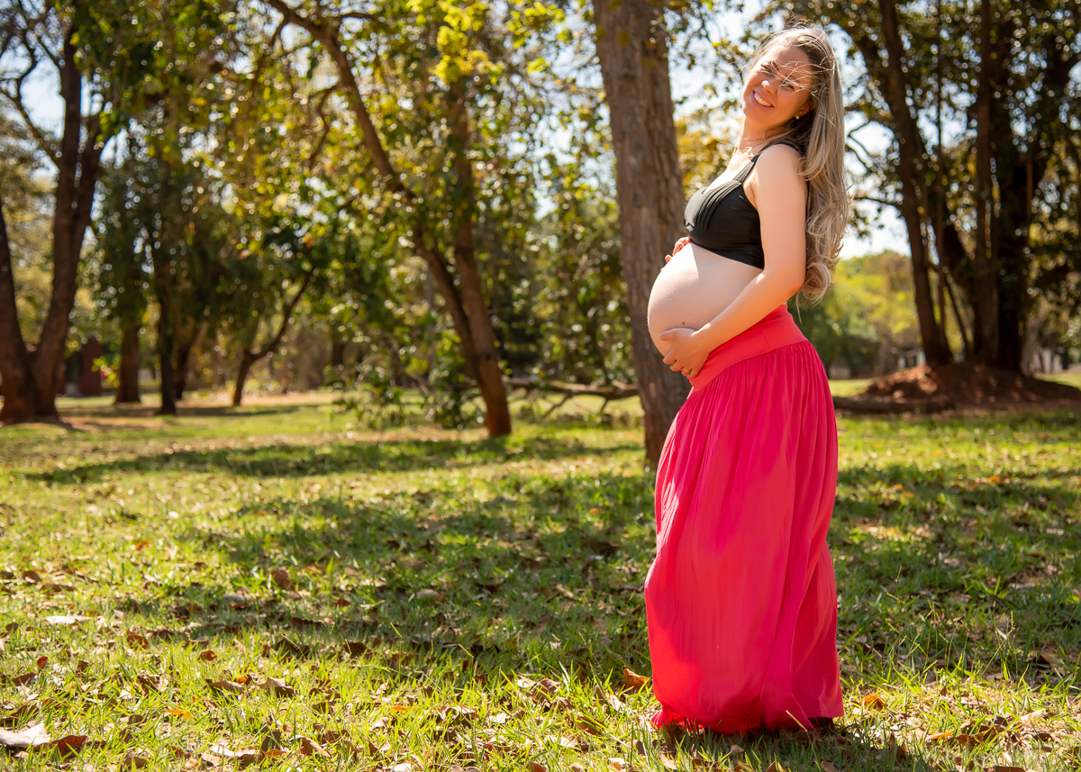 Ensaio de gestante de Gisele e Everton, a gestante com sua saia laranja e um top preto, posando de lado, de pé com as  mãos embaixo da barriga e vento bagunçando os cabelos. Fotos feitas pelo fotógrafo Pedro Stanke, em Campo Grande-MS. 
