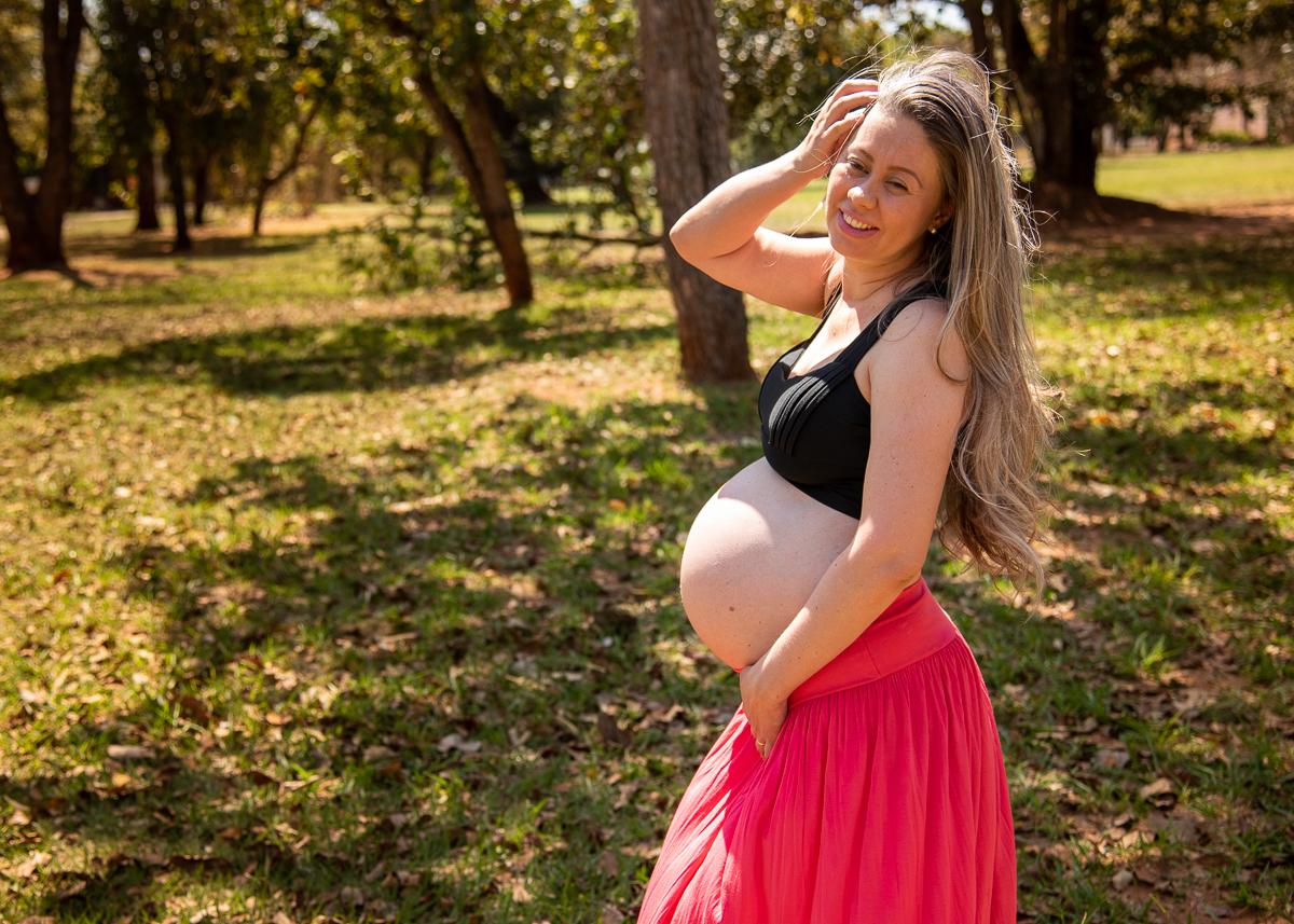 Ensaio de gestante de Gisele e Everton, a gestante com uma saia laranja e um top preto, de pé com uma das mãos nos cabelos e outra  na barriga. Fotos feitas pelo fotógrafo Pedro Stanke, em Campo Grande-MS. 