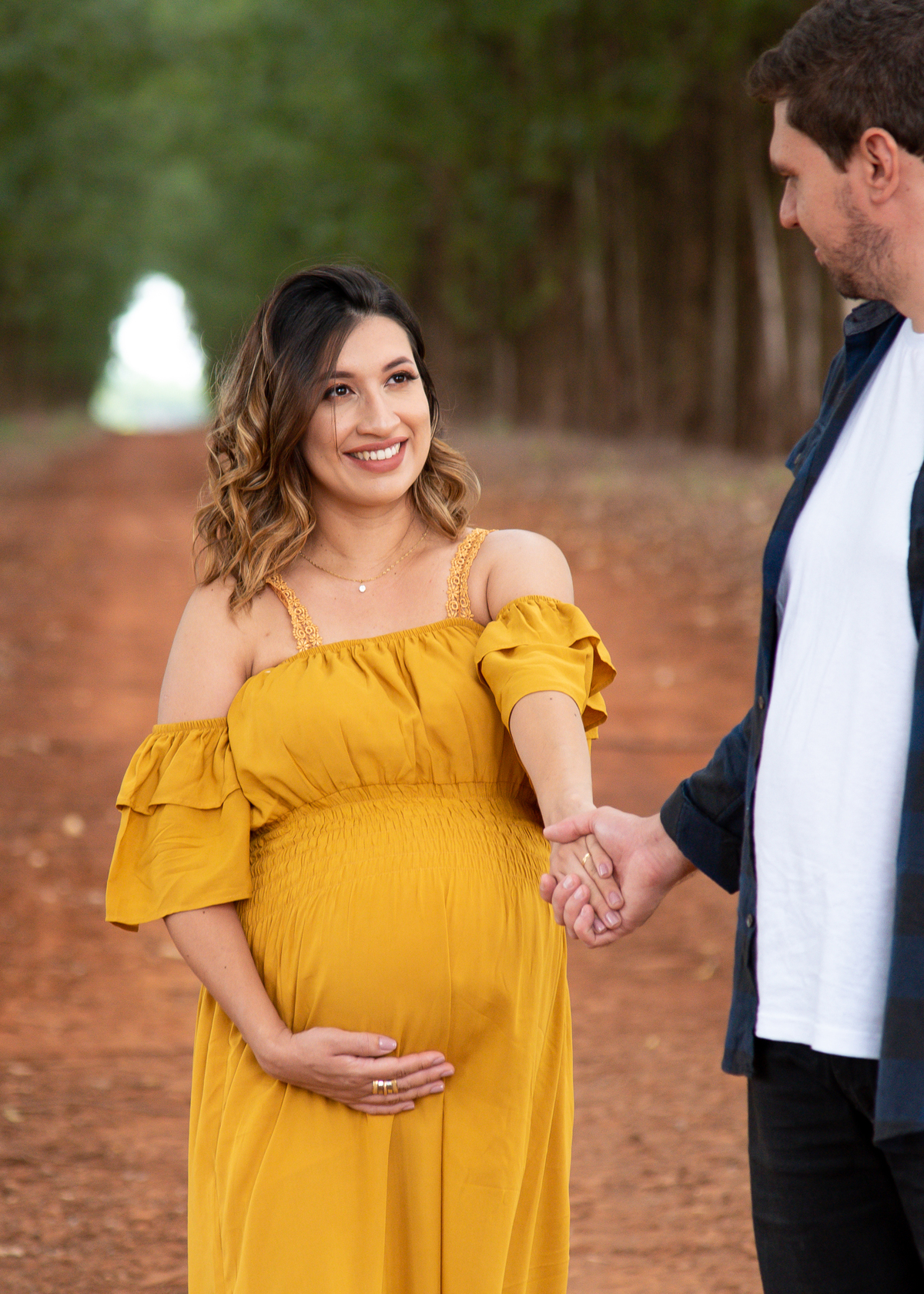 Ensaio Gestante, Donna e Allan, em uma estrada com eucaliptos. A gestante segurando a mão do pai e olhando para ele, e ele esta de lado, no meio da estrada e se olhando e sorrindo. Fotos feitas em Campo Grande-MS, por Pedro Stanke.