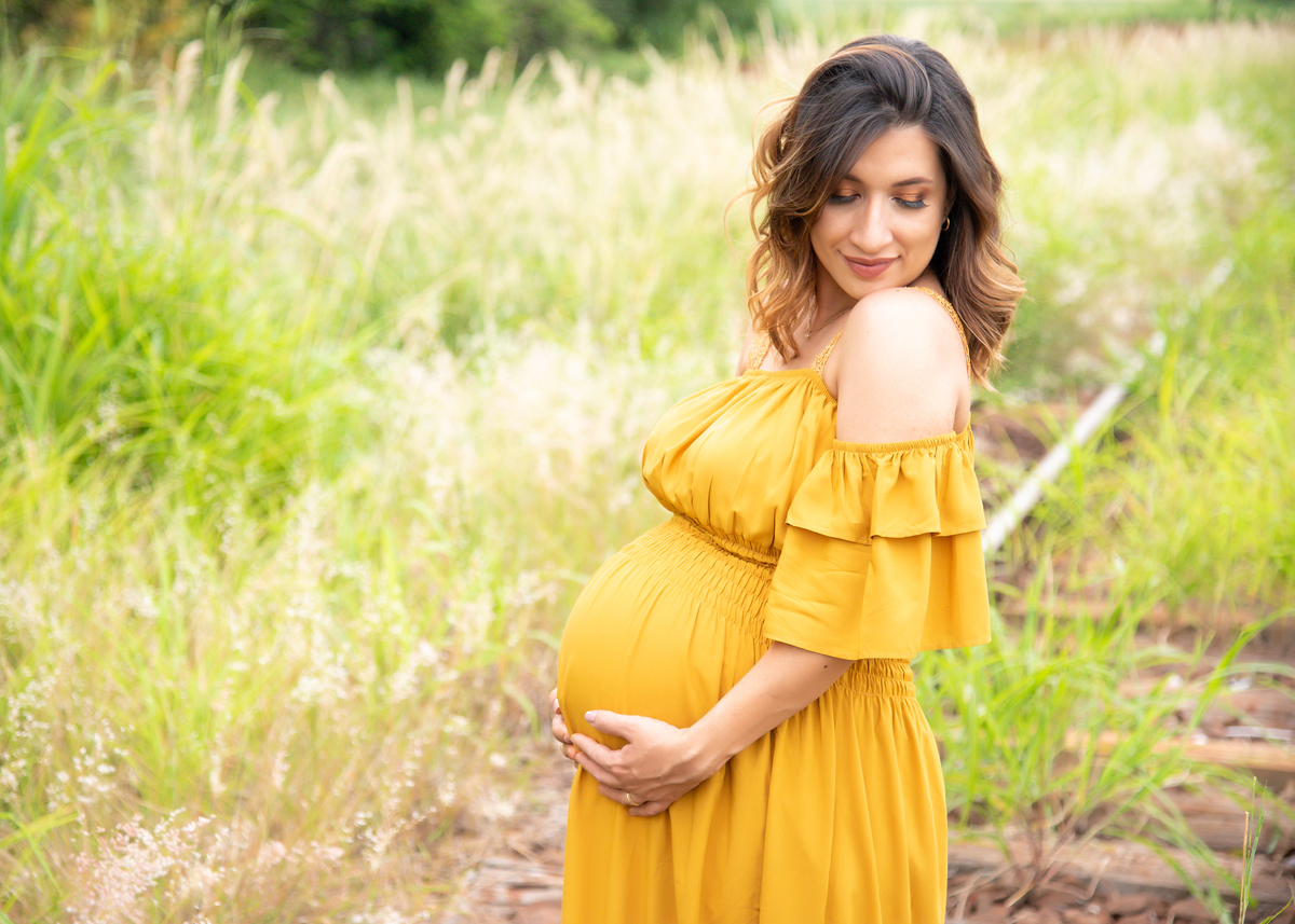 Ensaio Gestante, Donna e Allan, sobre os trilhos da estrada de ferro a gestante sozinha com as mãos sob a barriga, e olhando para baixo e de lado com leve sorriso. Fotos feitas em Campo Grande-MS, por Pedro Stanke.