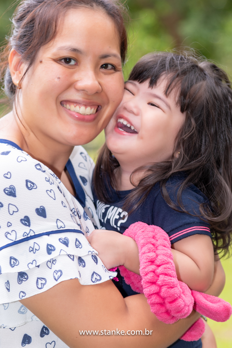 Ensaio Luísa de 2 anos, Um close da aniversariante no colo da sua mãe, ambas com lindos sorrisos, e com rostos coladinhos e o seu coelhinho no braço. Fotos realizadas no Carandá Bosque, pelo fotógrafo Pedro Stanke. 