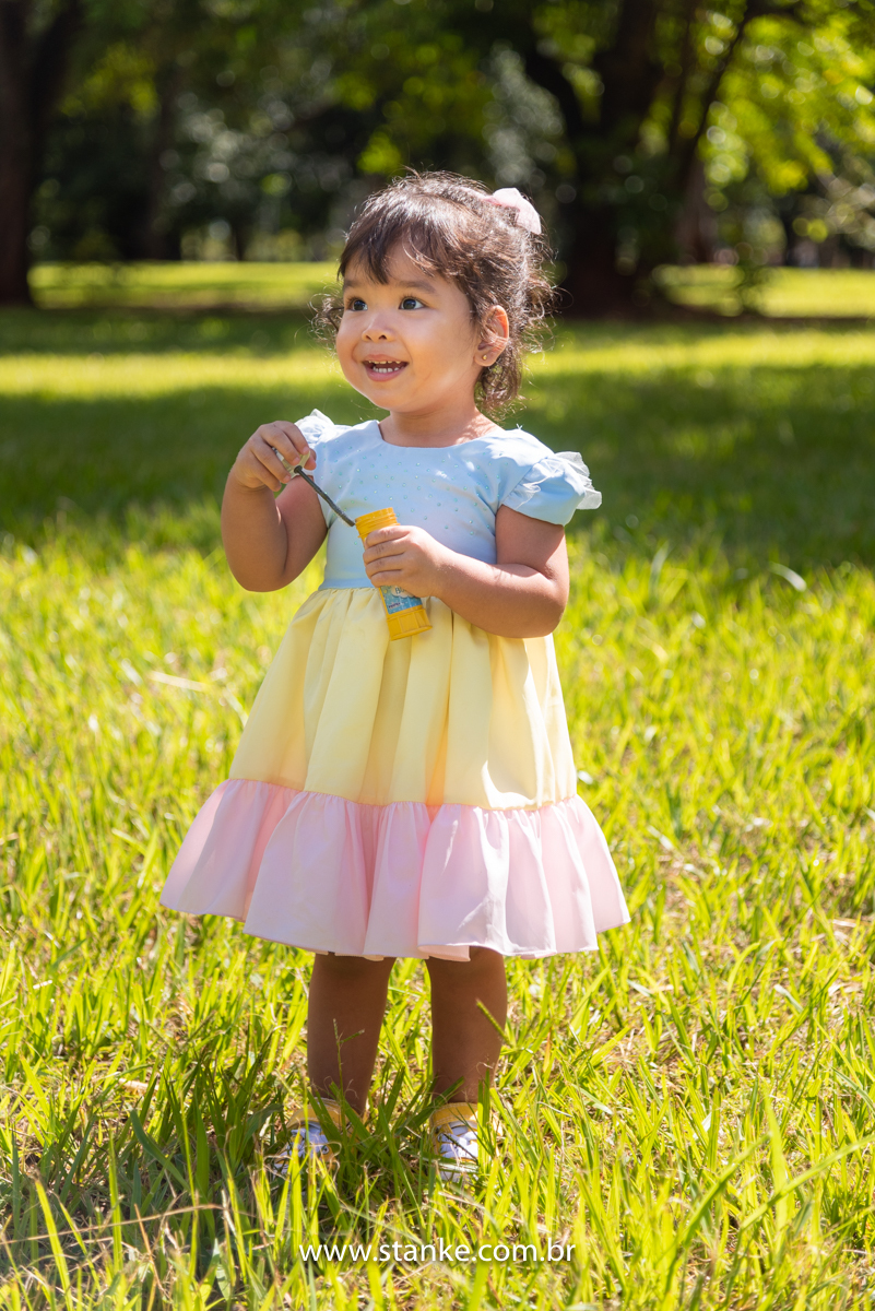 Ensaio infantil da Clara com 2 anos, Aniversariante, com seu vestido colorido,  fazendo bolhinhas de sabão e com lindo sorriso. Fotos feitas no Bosque da Paz, pelo fotógrafo Pedro Stanke. 