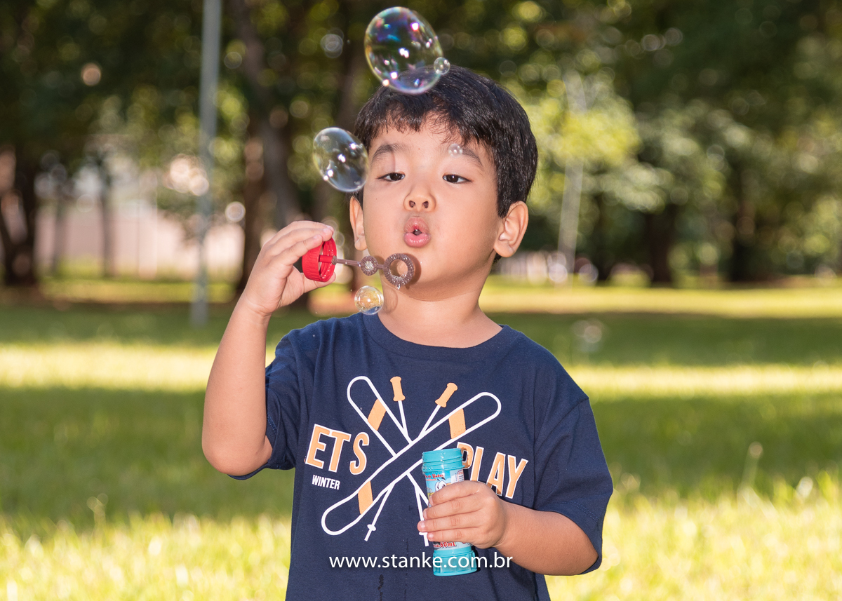 Ensaio infantil do Davi com 4 anos, Aniversariante, soprando forte para fazer enormes bolhinhas de sabão. Fotos feitas no Bosque da Paz, pelo fotógrafo Pedro Stanke. 