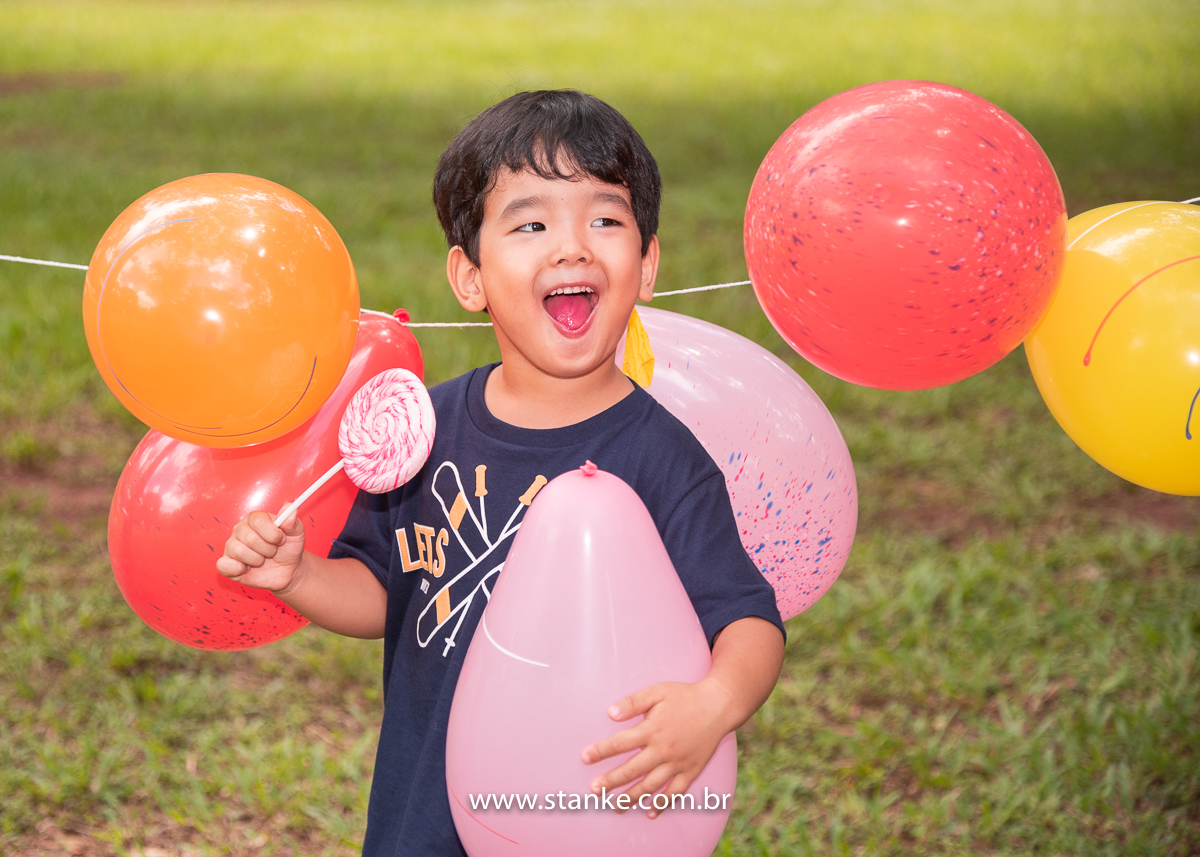 Ensaio infantil do Davi com 4 anos, Aniversariante, junto aos balões e segurando um dos balões e com seu enorme pirulito colorido e com lindo sorriso. Fotos feitas no Bosque da Paz, pelo fotógrafo Pedro Stanke. 