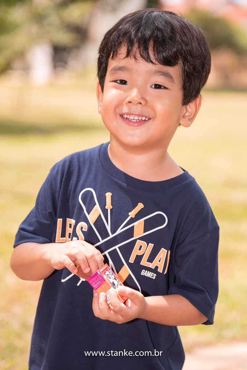 Ensaio infantil do Davi com 4 anos, Aniversariante, olhando para câmera e com um lindo sorriso, enquanto segura a caixinha de estranhos. Fotos feitas no Bosque da Paz, pelo fotógrafo Pedro Stanke. 