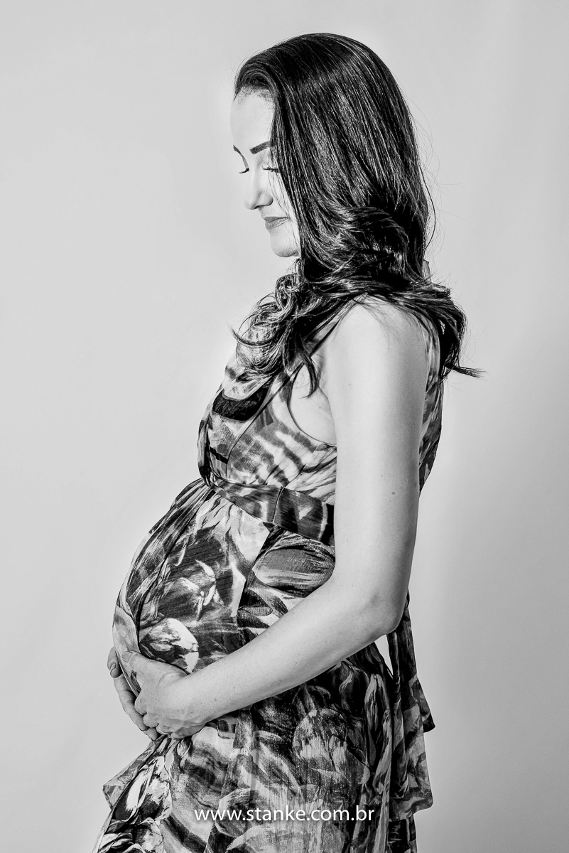 Ensaio gestante em estúdio, no estúdio Stanke Fotografia, foto preto e branco, gestante com vestido longo e estampado de azul, com as mãos na barriga e olhando para frente, com lindo sorriso. Fotos realizadas pelo fotógrafo Pedro Stanke.