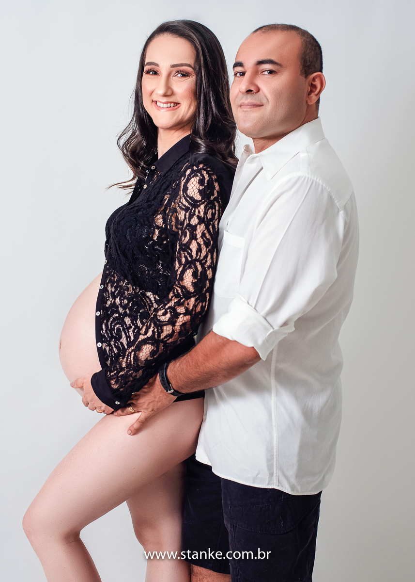 Ensaio gestante em estúdio, no estúdio Stanke Fotografia, gestante com blusa rendada e lingerie preta, com seu esposo abraçando por traz e olhando para câmera com lindos sorrisos. Fotos realizadas pelo fotógrafo Pedro Stanke.
