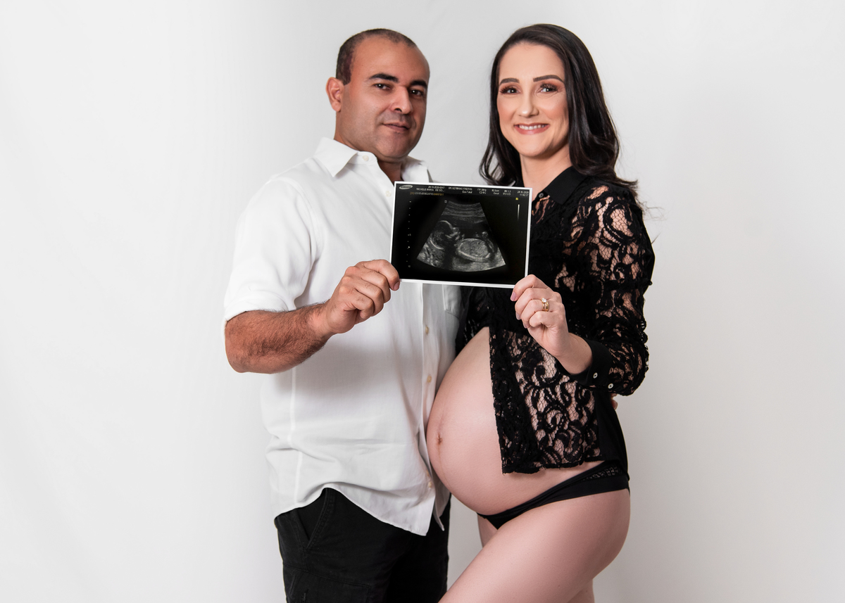 Ensaio gestante em estúdio, no estúdio Stanke Fotografia, gestante com blusa rendada e lingerie preta, com seu esposo ambos segurando a foto do ultra e olhando para câmera com lindos sorrisos. Fotos realizadas pelo fotógrafo Pedro Stanke.