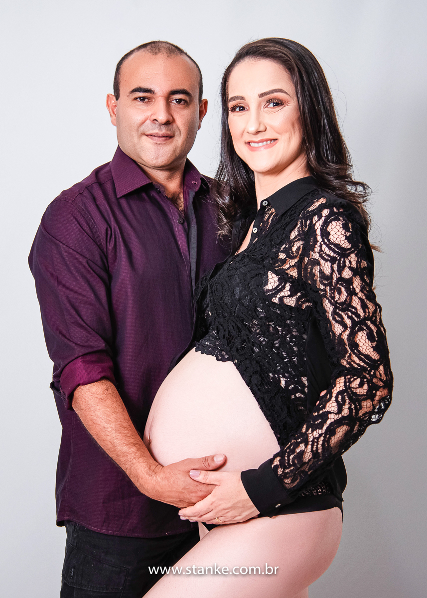 Ensaio gestante em estúdio, no estúdio Stanke Fotografia, gestante com blusa rendada e lingerie preta, com seu esposo e ambos com a com as mãos na barriga olhando para câmera com lindos sorrisos. Fotos realizadas pelo fotógrafo Pedro Stanke.