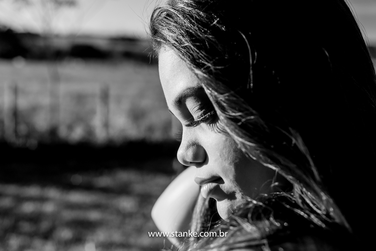 Ensaio 15 anos externo, um close bem fechado em preto e branco, da aniversariante com olhar abaixado e de lado, e com uma das mãos no nos cabelos. Fotos realizadas Estância Mariana perto Campo Grande-MS. Fotógrafo Pedro Stanke.