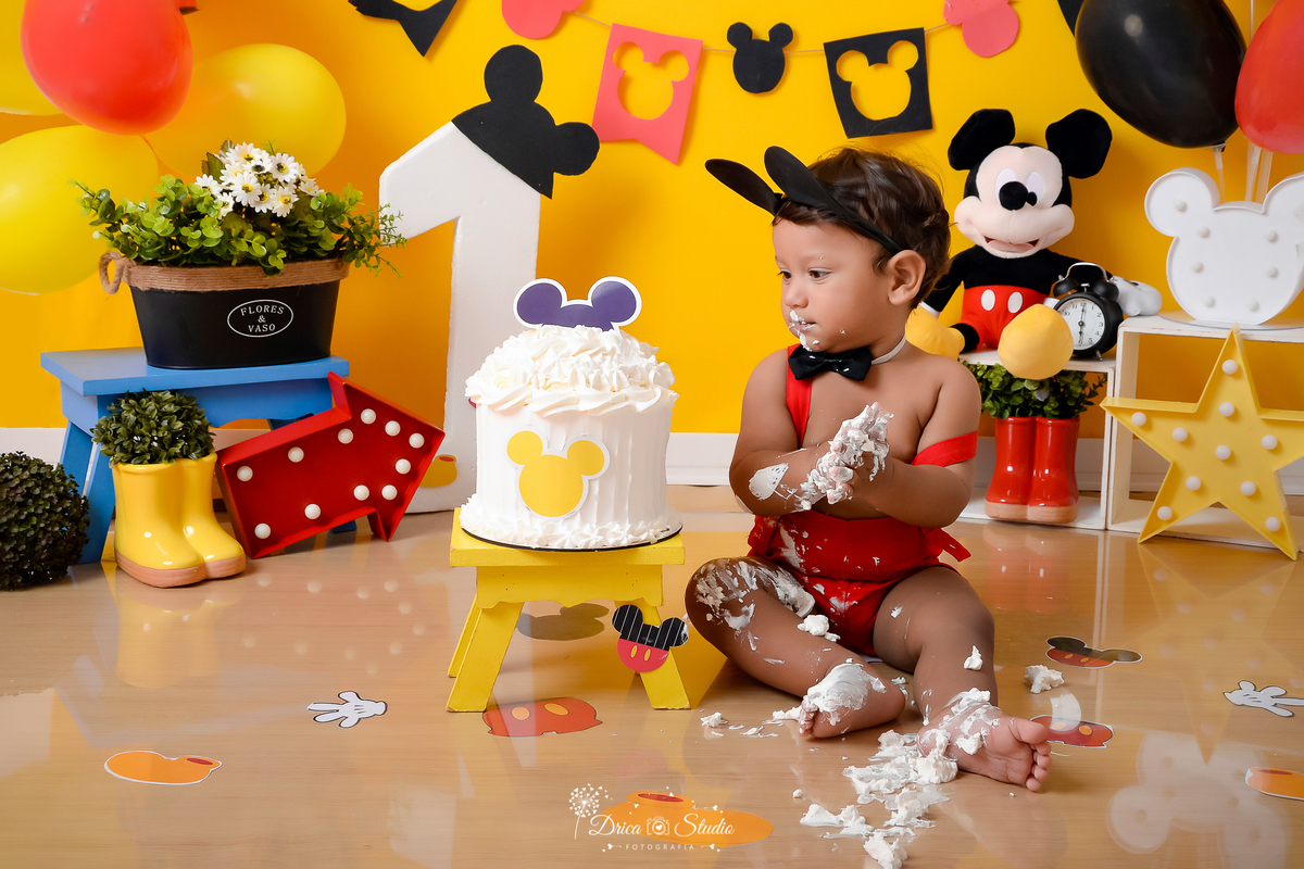 Drica Studio - Drica Studio Fotografias - Drica Studio Xinguara Pará - Ensaio de 1 ano - Smash the cake - Cenário Mickey mouse - urso - balões vermelho - amarelo - preto - fundo amarelo - roupa do Mickey - bolo do Mickey - comendo bolo 
