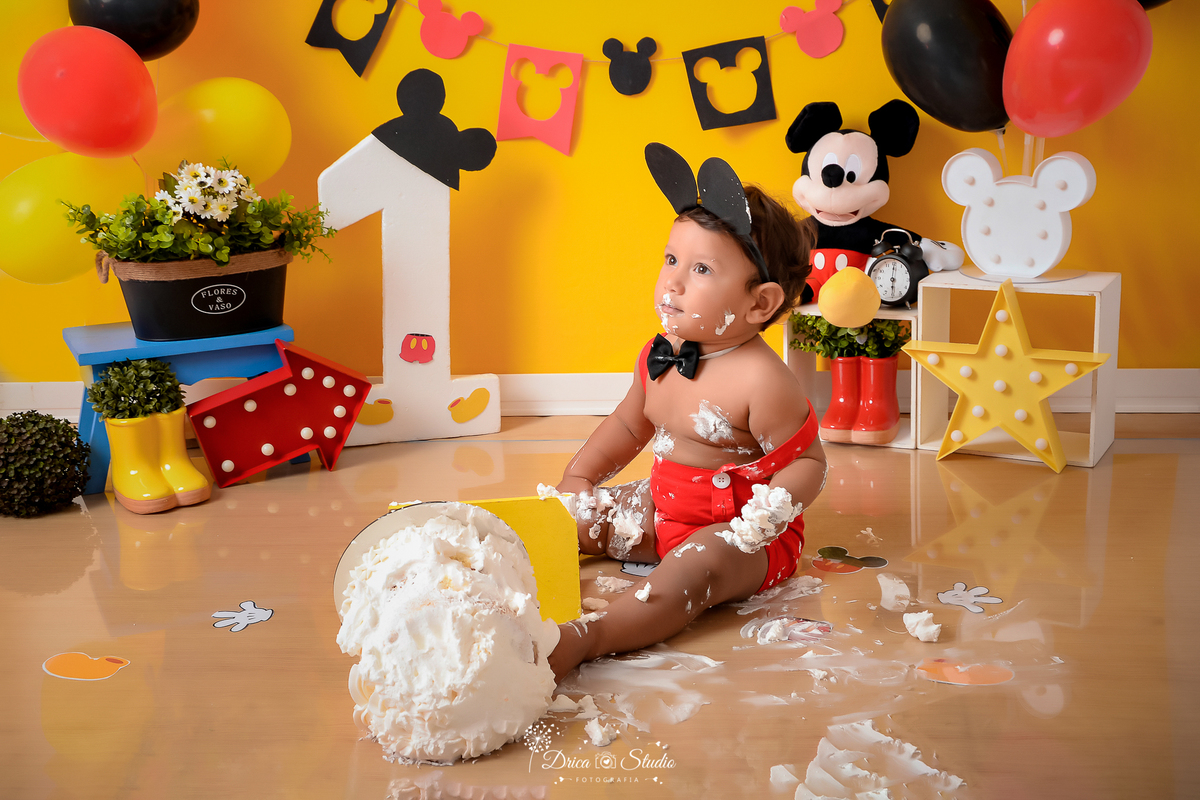 Drica Studio - Drica Studio Fotografias - Drica Studio Xinguara Pará - Ensaio de 1 ano - Smash the cake - Cenário Mickey mouse - urso - balões vermelho - amarelo - preto - fundo amarelo - roupa do Mickey - esmagando o bolo 