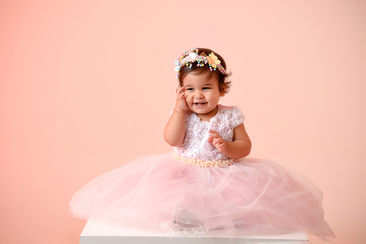 Drica Studio - Drica Studio Fotografias - Xinguara Pará - ensaio feminino - acompanhamento mensal - bebe de 1 ano - cenário rosa - batendo palmas - vestido de tule - tiara de borboletas - sorridente - mão no rosto 