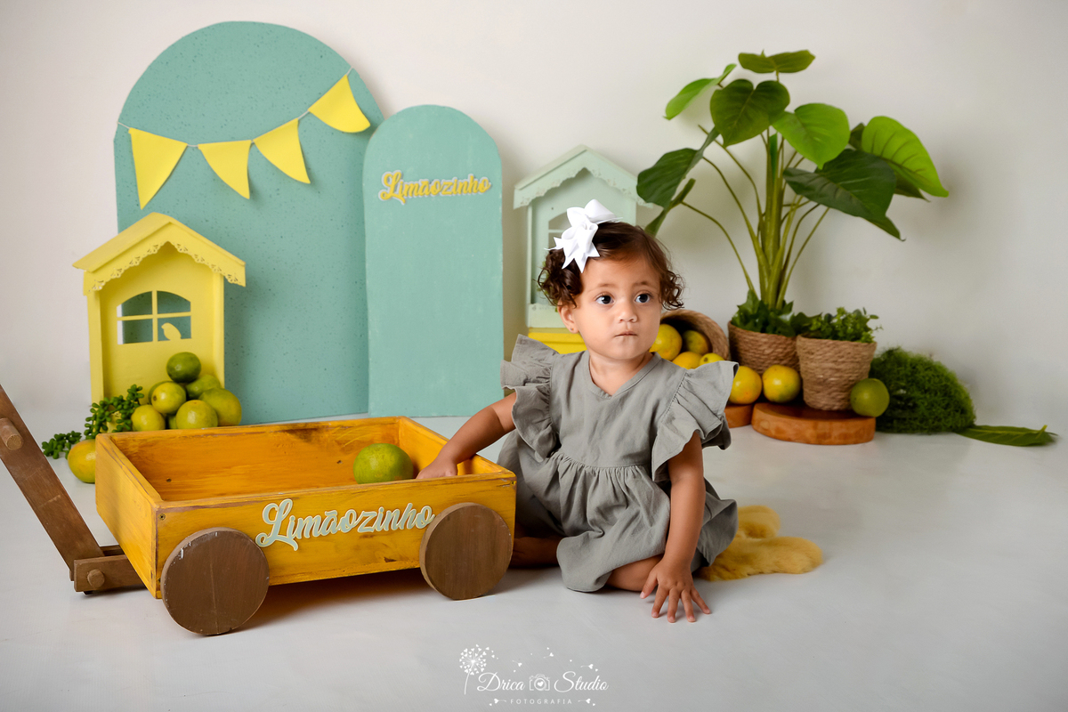 drica studio - ensaio infantil fotográfica - cenário de frutas cítrica - verde e amarelo - menina sentada no chão - xinguara