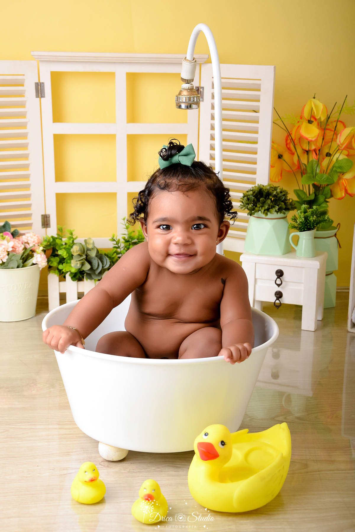 drica studio - ensaio fotográfico - xinguara - menina sorrindo dentro de banheiro - com cômoda branca, vaso de flores verdes - janela branca - fundo amarelo 