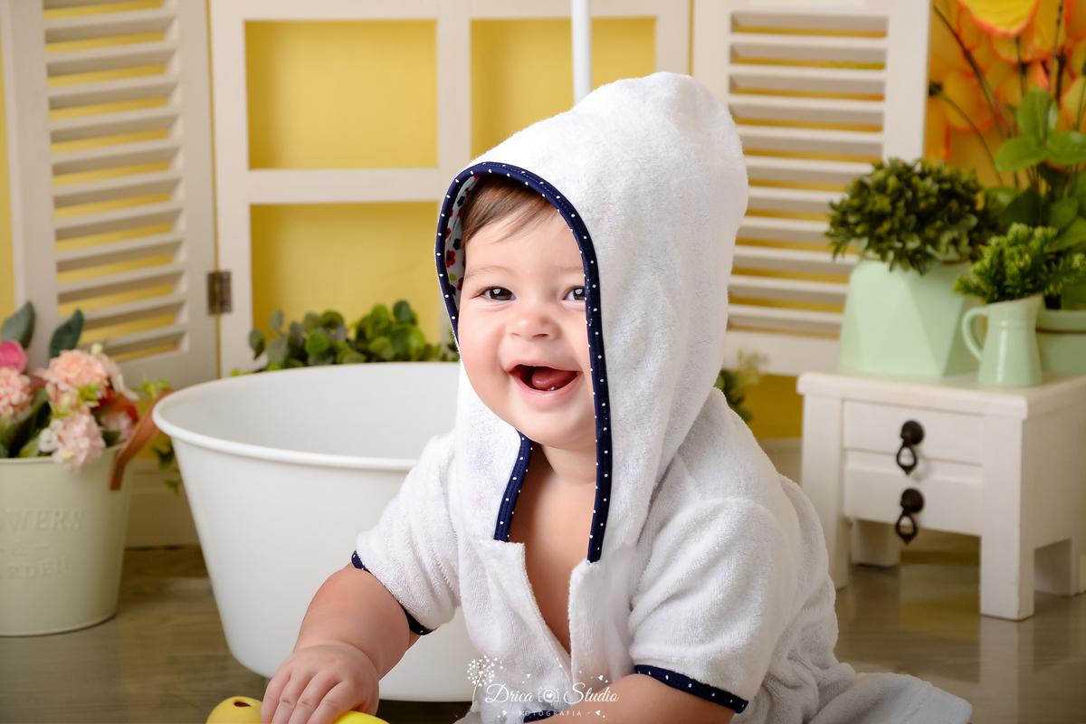 drica studio - ensaio fotográfico - xinguara - menina vestindo roupão branco com detalhes azul escuro - banheira branca - mini cômoda branca com vazos verdes - janela branca - cenário com fundo amarelo