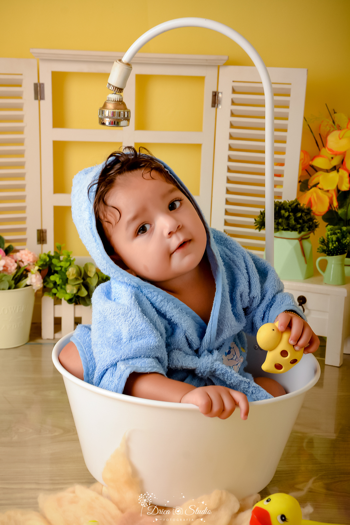 drica studio - ensaio fotográfico - xinguara - menino vestindo roupão azul claro, segurando patinho amarelo de borracha - janela ao fundo - cenário com fundo amarelo