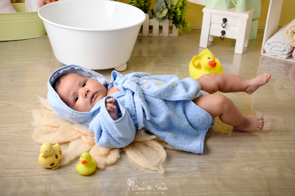 drica studio - ensaio fotográfico - xinguara - bebê deitado em tapete felpudo vestindo roupão azul claro - banheira branca - cômoda branca - patinhos amarelos - piso amadeirado