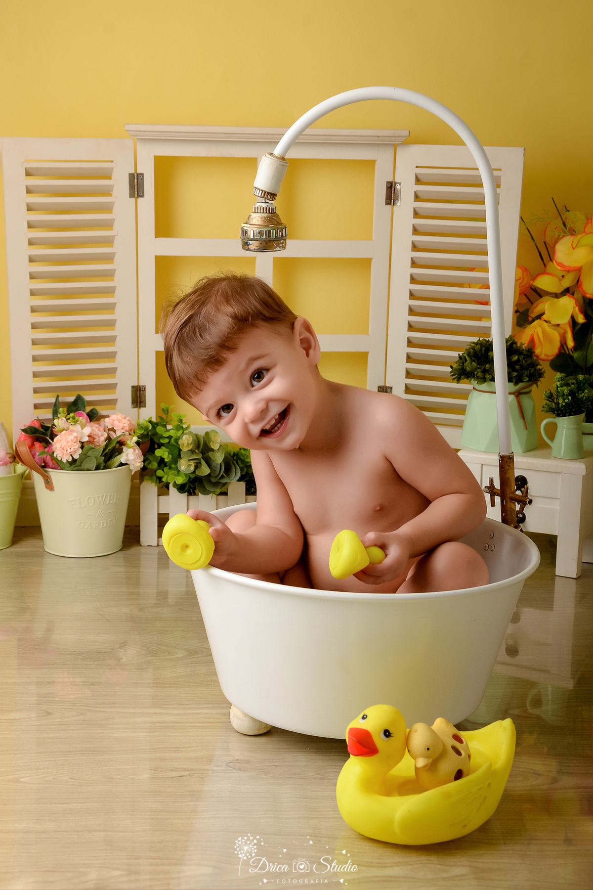 drica studio - ensaio fotográfico - xinguara - menino banhando em banheira branca, brincado com dois patinhos amarelos - janela com jardineira branca - balde branco com flores rosa - cenário com fundo amarelo
