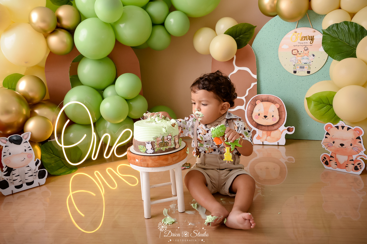 drica studio - ensaio fotográfico - xinguara - smahs the cake safari - menino sentando no chão enviando a mão no bolo - bichinho safari baby - one - painel verde claro e marrom - bolo tema safari