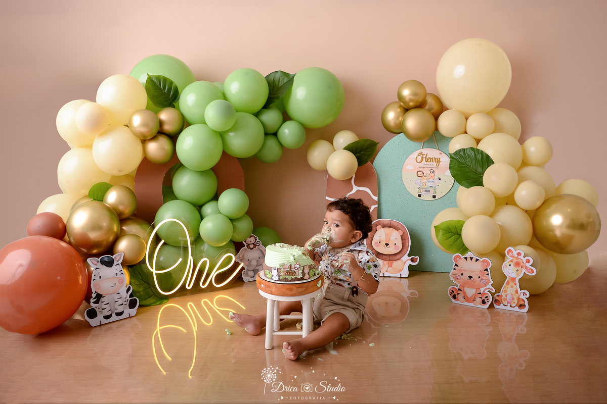 drica studio - ensaio fotográfico - xinguara - smahs the cake safari - baloes marfim, verde, marrom e dourado - banquinho branco - bolo verde - menino sentado no chão comendo bolo