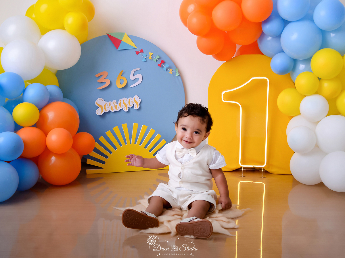 drica studio - ensaio fotográfico - smash the cake - xinguara - 365 sorrisos - um de led - painel azul - painel amarelo - solzinho - bebê vestindo roupa branca sentado no chão - tapete felpudo - piso amadeirado