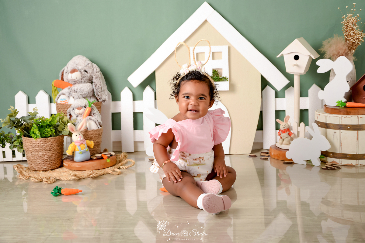 drica studio - ensaio fotográfico infantil - xinguara - páscoa - bebê sentada no chão - tiara de coelho - casa de coelho - cesto de palha - coelhos - cenoura - fundo verde - balde de madeira branco 