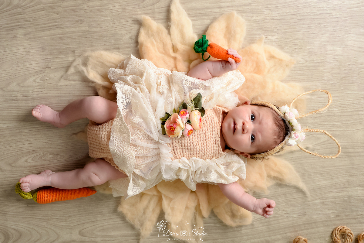 drica studio - ensaio fotográfico infantil - xinguara - páscoa - bebê deitada em tapete felpudo - cenoura - roupa de renda - piso amadeirado - tiara de coelho 