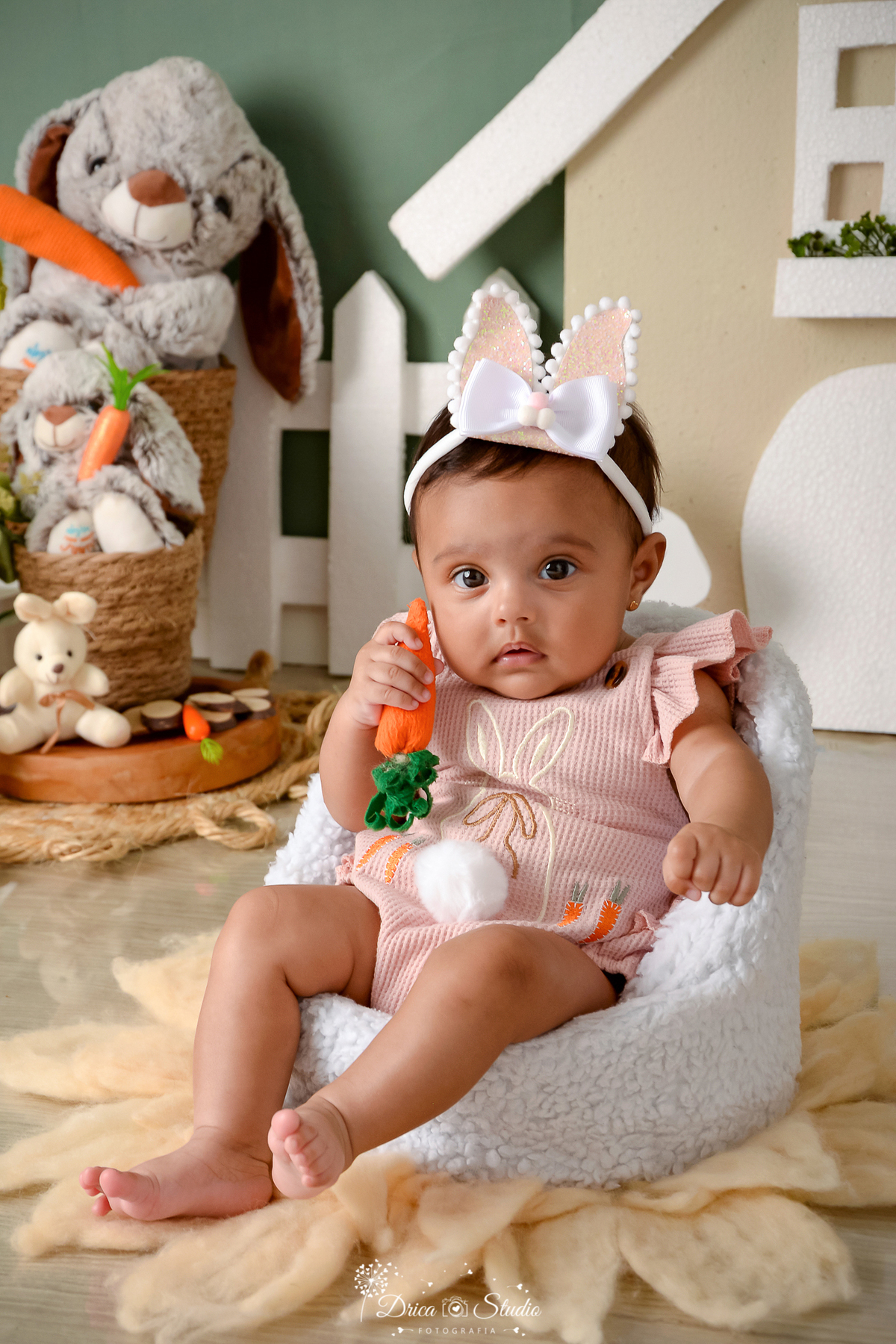 drica studio - ensaio fotográfico infantil - xinguara - páscoa - bebê segurando cenoura - tiara de coelho - coelho - cerca branca - piso amadeirado - poltrona branca