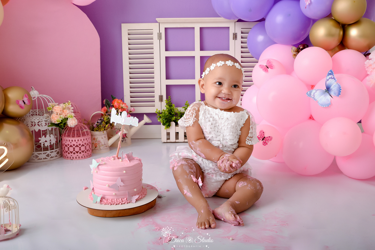 Drica studio - ensaio fotográfico - xinguara - jardim encantado - smash the cake - bolo rosa - bory de renda branco - borboleta azul - janela branca - gaiola branca e rosa - regadores - painel rosa - bebê sorridente suja de glacêr
