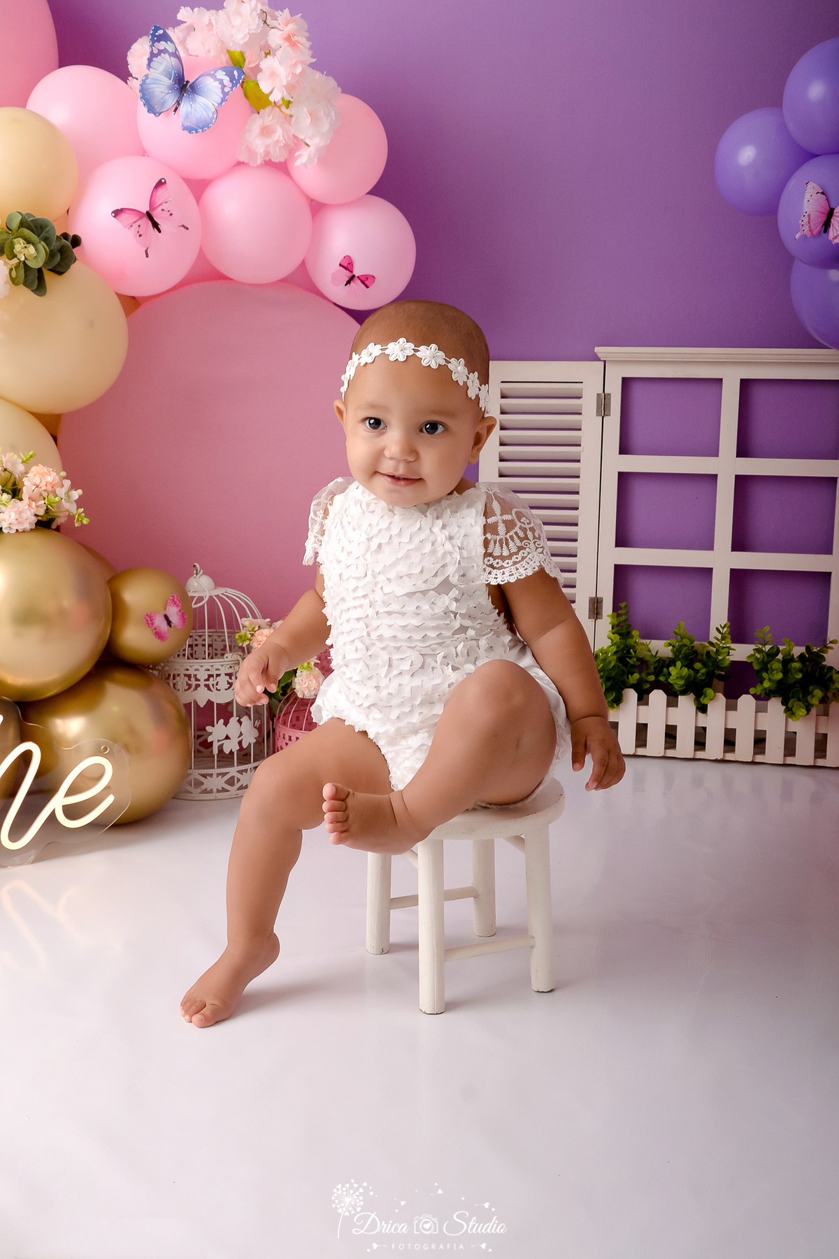 Drica studio - ensaio fotográfico - xinguara - jardim encantado - smash the cake - bebê sentada em banquinho branco vestida em bory de renda branco - one - janela com jardineira - gaiola branca - painel rosa - fundo lilás