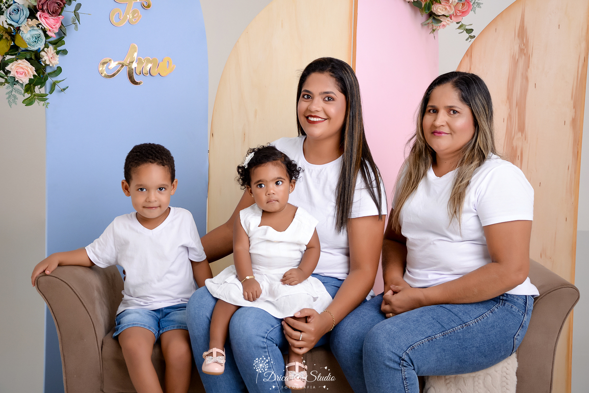drica studio, ensaio fotografico, xinguara, dia das mães, avó, mãe e um casal de filhos, divam marrom, painel azul, rosa e amadeirado, arranjo de flores, camiseta branca e calça jeans, menina vestindo vestido branco