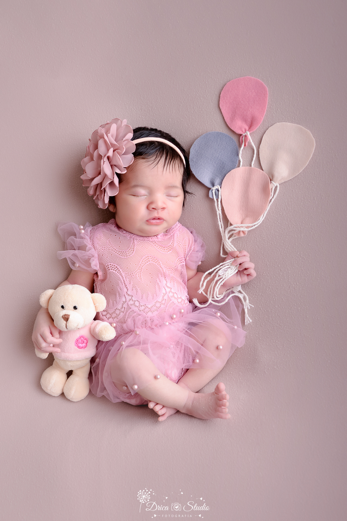 drica studio - ensaio fotográfico - xinguara - newborn menina - bebê dormindo segurando urso rosa de pelucia com a mão esquerda e balões de feltro com a mão direita - vestido de renda rosa com pérolas rosa - tiara de flor - fundo bege