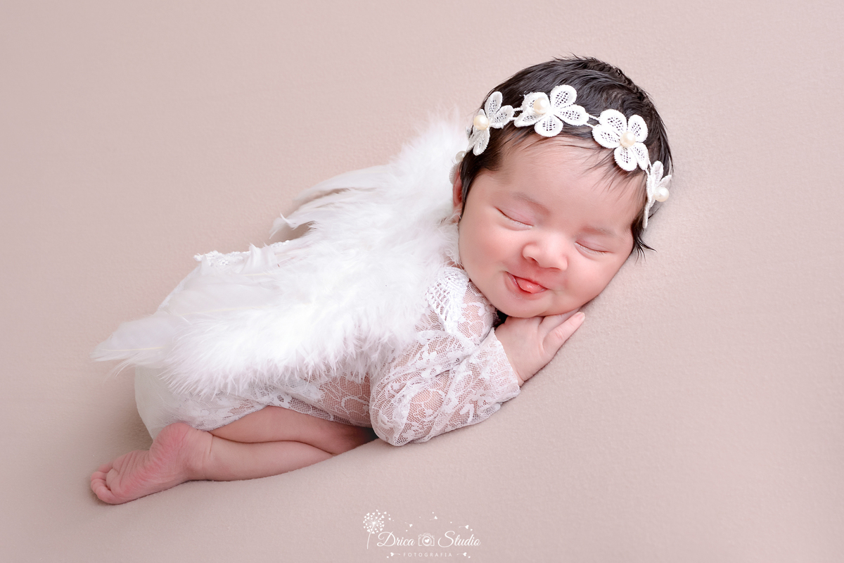 drica studio - ensaio fotográfico - xinguara - newborn menina - bebê dormindo vestinto body de renda branco, com asa de anjo e tiara de flores brancas na cabeça. - fundo bege