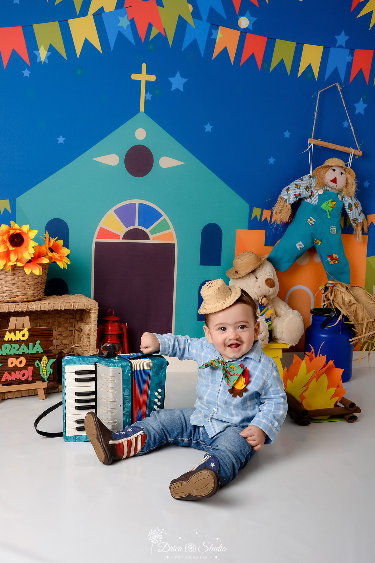 Drica studio - ensaio fotográfico infantil- xinguara - festa junina - fundo com tema junino - bebê com roupa junina e chapel de palha - sanfona - cesto de palha com flores - ursinho branco com chapel de palha - espantalho - latão de leite azul - fogueira 