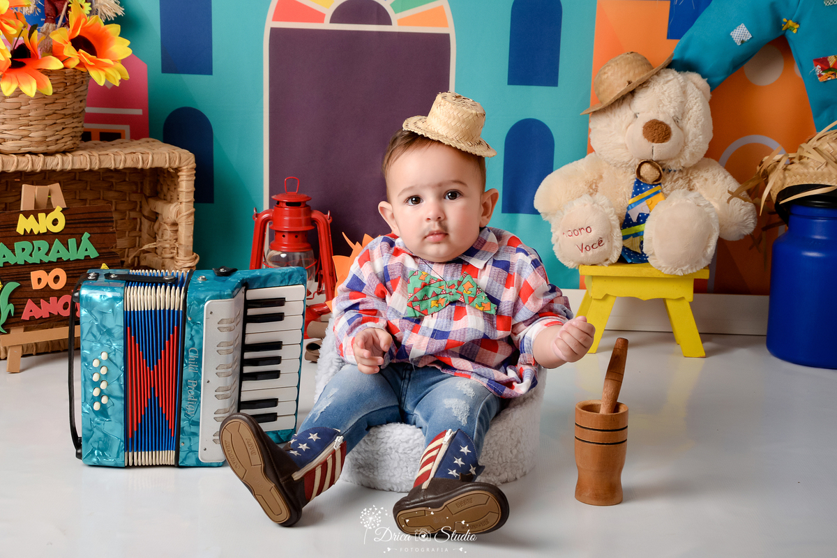 Drica studio - ensaio fotográfico infantil- xinguara - festa junina - sanfona - camisa infantil xadrez azul com vermelho - calça jeans infantil - ursinho branco com chapéu de palha - latão de leite azul - lampião vermelho - chapéu de palha