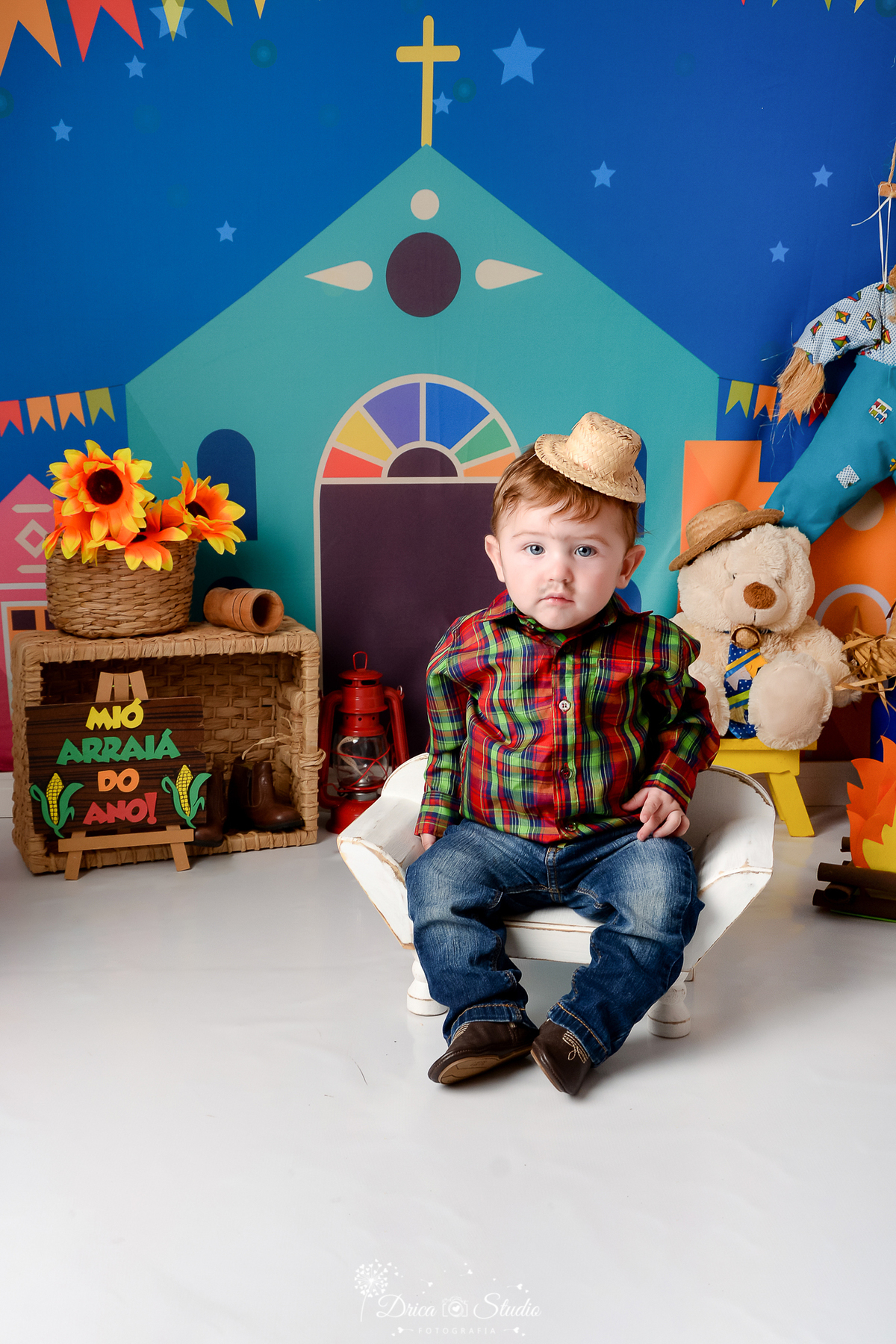 Drica studio - ensaio fotográfico infantil- xinguara - festa junina - bebê vestindo camisa xadrez vermelha e verde - chapéu de palha - ursinho branco com chapéu de palha - cesto de palha com girassois - banquinho branco - fundo com tema junino 
