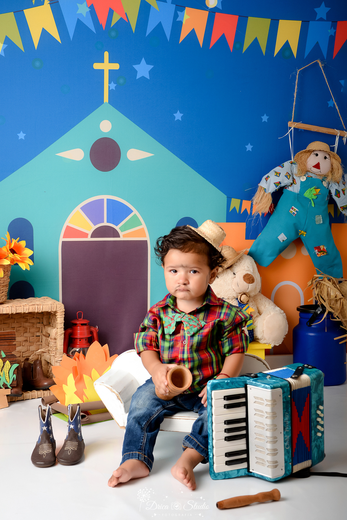 Drica studio - ensaio fotográfico infantil- xinguara - festa junina - menino sentado em banquinho branco - camisa infantil xadrez - fundo tema junino - lampião vermelho - espantalho - ursinho branco com chapéu de palha - latão de leite azul 