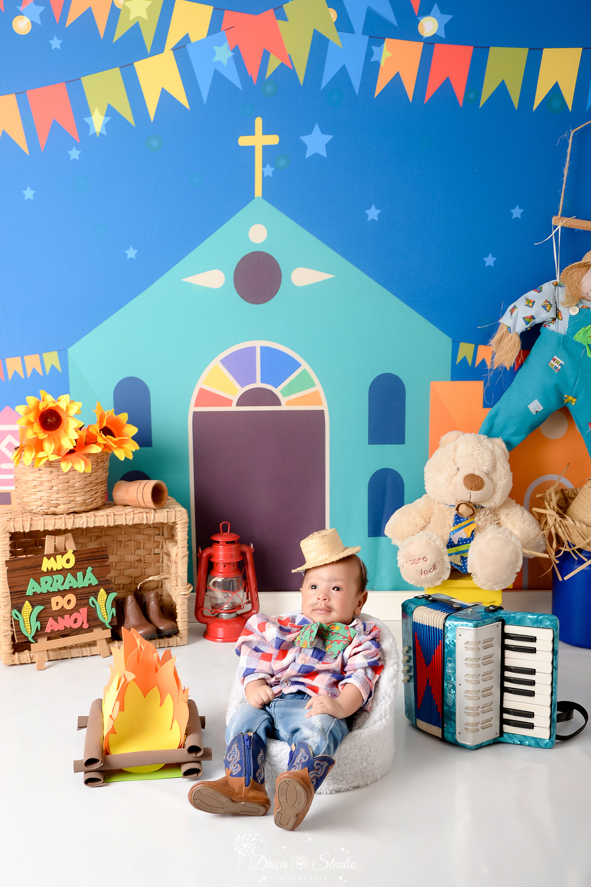 Drica studio - ensaio fotográfico infantil- xinguara - festa junina - bebê sentado poltrona branca - ursinho branco - espamtalho - cesto de palha com girassois - lampião  vermelho - fundo tema junino - sanfona - latão de leite azul - lampião vermelho 