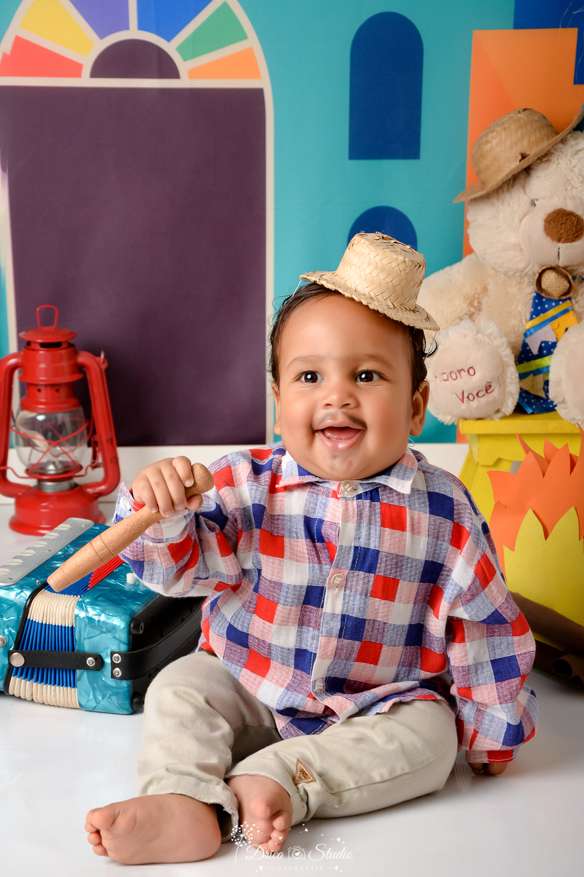 Drica studio - ensaio fotográfico infantil- xinguara - festa junina - bebê sorridente vestindo camisa xadrez e chapéu de palha - lampião vermelho - urso branco - fogueira - fundo colorido