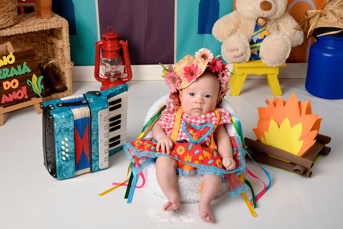 Drica studio - ensaio fotográfico infantil- xinguara - festa junina - bebê vestida em vestido junino - fogueira - latão de leite azul - ursinho branco com chapéu de palha - sanfona azul - lampião vermelho - cesto de palha