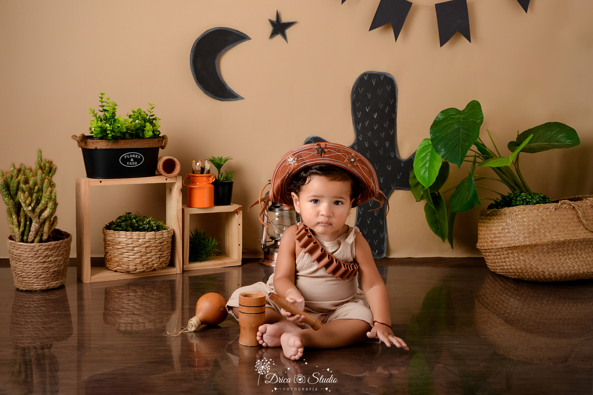 drica studio - ensaio fotografico infantil - tema sertão nordestino - cestos de palha - vaso preto com arbusto dentro - fundo de cordel - cacto - chapéu de cordel - piso amadeirado - nicho de madeira -  maquinho bege - pilão de madeira